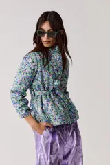 Chaqueta capitoneada con estampado floral y terminación metálica, cuello alto, cierre frontal escondido, cinturón para atar y bolsillos laterales.