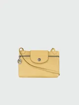 Mini bolso cruzado de cuero amarillo, con solapa frontal con logo grabado, cierre de cremallera y correa ajustable. Incluye un dije metálico circular colgante con el logo de la marca.
