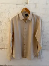 Camisa de lino color beige, de manga larga, con cuello clásico y cierre frontal abotonado.