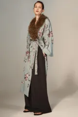 Kimono de largo midi en color verde grisáceo, con cuello de solapas amplias en pelo sintético marrón. Presenta mangas largas acampanadas, cierre frontal con cinturón ajustable del mismo tejido y un delicado estampado floral bordado en toda la prenda.