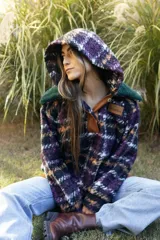 Buzo tipo canguro de corte oversize, confeccionado en paño de lana con diseño de rayas horizontales en tonos marrón, blanco y azul. Presenta una capucha amplia y un cuello de piel sintética en color verde oscuro.