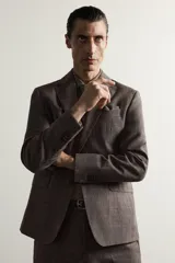 Blazer regular fit de Zara, confeccionada en tejido de lino y lana con diseño a cuadros en tonos marrones y grises. Cuenta con solapas de muesca, cierre frontal de un botón y bolsillos con solapa en la cadera.
