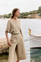 Top de punto color beige con cuello barco y mangas cortas anchas tipo murciélago. Cuenta con cintura entallada con ribete elástico y un cinturón fino de cuero sintético marrón con hebilla metálica dorada.
