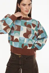 Sweater de tejido de punto con diseño geométrico multicolor en tonos marrón, celeste, verde y crudo. Presenta cuello redondo, mangas largas abullonadas y puños y ruedo elásticos en color marrón.