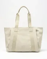 Cartera tipo tote color beige con asas de hombro decoradas con el texto impreso de la marca, bolsillo frontal y parche circular grabado con el logotipo en la parte inferior.
