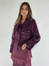 Chaqueta tipo camisa de terciopelo color borgoña, con cuello clásico, cierre frontal con botones, dos bolsillos con solapa en el pecho y detalle de estrella metálica en uno de ellos. De corte recto y mangas largas.