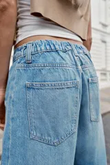 Jeans baggy de tiro medio con pernera holgada, diseño de cinco bolsillos y bajo acabado en vuelta. Cuenta con cintura elástica en la espalda y cierre frontal con cremallera y botón.