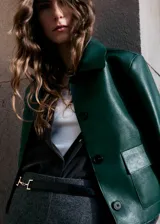 Chaqueta verde oscuro de efecto piel con cuello camisero, manga larga, dos bolsillos de parche con solapa en el frente y cierre delantero de botones ocultos.
