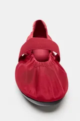 Zapato tipo bailarina de estilo deportivo en color rojo, con tira ancha elástica y fruncidos en el empeine, talonera en contraste y suela plana engomada con punta redonda.