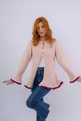 Saco rosado de lana merino y acrílico, con punto acanalado, corte recto, mangas largas acampanadas con ribete en color crema y bordó, y cierre frontal con lazos de crochet.