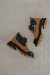 Botas Chelsea de cuero color camel con paneles laterales elásticos negros y puntera de charol negro. Tienen una suela track gruesa en negro y camel.