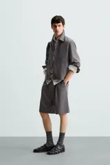 Bermuda de corte relajado color negro, con pliegues frontales, cierre de cremallera y botón, bolsillos laterales y bolsillos traseros.