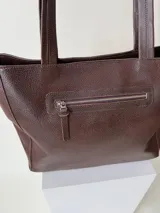 Cartera tipo shopper de cuero marrón texturado, con doble asa de hombro y un bolsillo frontal amplio con cierre de imán.