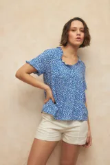 Blusa de manga corta con estampado floral blanco sobre fondo azul, con cuello redondo detallado con pequeños volados y corte holgado.