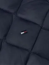 Chaleco azul marino acolchado con relleno de plumón, sin cuello y cierre a presión. Cuenta con el logo de Tommy Hilfiger bordado en el pecho.