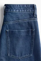 Pantalón jean de denim azul, tiro alto, con diseño wide leg de cinco bolsillos y cierre frontal con botón y cremallera.