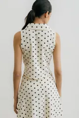 Chaleco blanco con estampado de lunares negros, cuello camisero y cierre frontal con broches metálicos.