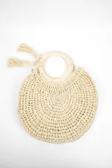 Cartera de mano beige, de rafia tejida con forma semicircular y asas redondas. Incluye dos borlas decorativas.