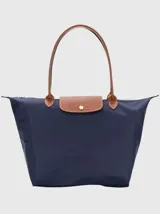 Bolso tote plegable color azul marino, con cuerpo de nylon y solapa de cuero marrón. Posee dos asas de mano de cuero marrón y cierre superior con broche dorado.