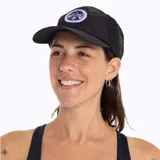 Gorra tipo trucker color negro con paneles laterales de malla. Presenta un parche circular bordado en el frente con el logo de Merrell, un diseño de montañas y una flor edelweiss.
