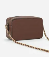 Cartera bandolera pequeña de textura granulada, con cierre superior de cremallera y correa de cadena entrelazada con material sintético. Presenta un diseño rectangular con placa metálica decorativa en el frente.