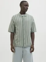 Polo de punto verde con rayas verticales blancas, corte relajado, cuello tipo camisa, cierre con botones y mangas cortas.