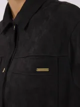 Campera de estilo camisero con efecto gamuzado, color beige, de corte recto y holgado. Presenta cuello clásico, cierre frontal con botones, mangas largas con puños abotonados y bolsillos frontales aplicados.