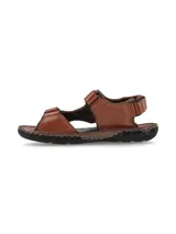 Sandalias de cuero color marrón, con diseño cerrado en el talón, tiras anchas en los laterales y cierre con velcro en el empeine y la parte frontal. Suela de goma negra con costuras visibles.