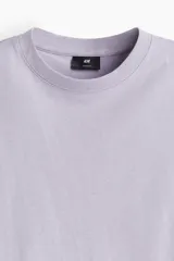 Remera de punto de algodón pesado, color lila claro, con cuello redondo ribeteado, hombros caídos y bajo recto. Corte holgado.