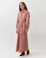 Vestido camisero largo de algodón con estampado a cuadros en tonos rojo y blanco, cuello clásico, mangas largas abullonadas y cinturón ajustable del mismo género.