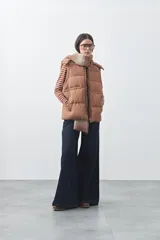 Chaleco puffer color tostado con diseño acolchado, capucha desmontable y cierre frontal. Cuenta con bolsillos laterales funcionales y un corte recto versátil.