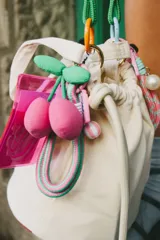 Llavero multifuncional con tarjetero de acrílico fucsia translúcido, decorado con un dije de cerezas de tela en color fucsia y verde, y una correa de cuerda trenzada en tonos fucsia y verde con detalles en lila.