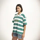 Remera tipo polo de manga corta, color verde oscuro, con cuello y abertura frontal. Presenta un estampado dorado en el pecho con el texto "PulauCrew" y un pequeño logo de corona de laurel bordado.