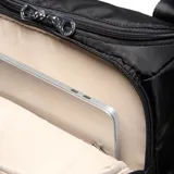 Bolso matero de diseño acolchado en color negro, con doble asa superior y correa ajustable extraíble. Presenta un compartimento principal con cierre doble, bolsillos externos con cierre y un parche circular con el logo de la marca en el frente.