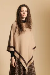 Poncho de silueta amplia y caída fluida, color beige con detalles de líneas en contraste color marrón en los bordes.