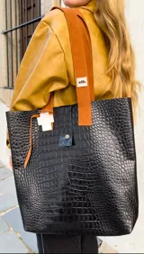 Bolso tote de cuero negro con textura de piel de cocodrilo, asas de cuero marrón y cierre con botón a presión.