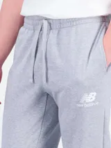 Pantalón deportivo New Balance modelo NBSSSWTPNT, color gris melange, con bolsillos laterales y puños elásticos en los tobillos. Cuenta con el logo bordado en la pierna izquierda.