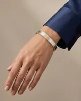 Pulsera tipo esclava rígida de acero inoxidable con baño de oro, que presenta un diseño bicolor con secciones lisas y una sección central texturizada.