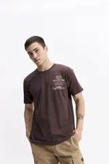 Remera de manga corta color marrón oscuro, con escote redondo y fit regular. Presenta un estampado frontal con texto en color amarillo y blanco.