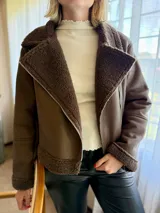 Campera de gamulán color marrón chocolate, con interior y detalles en corderito al tono. Presenta cierre frontal cruzado, cuello solapa amplio y bolsillos laterales con cierre metálico.