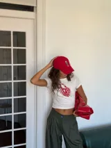Remera tipo baby tee de corte ajustado y largo cropped, color blanco con estampa frontal en forma de corazón rojo que incluye la frase 'Amar es no poseer'.