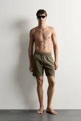 Short de baño largo en color beige, confeccionado en tejido técnico con tacto aterciopelado. Cuenta con cintura elástica ajustable con cordón, bolsillos laterales y detalle de bolsillo trasero, además de forro interior.