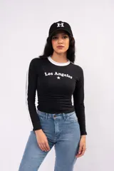 Remera de manga larga ajustada al cuerpo, color negro con cuello redondo blanco y franjas blancas laterales en las mangas. Presenta un estampado frontal con la inscripción 'Los Angeles' y una estrella pequeña.