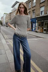 Jersey de punto gris jaspeado, de manga corta y escote redondo. El bajo presenta un acabado deshilachado o con flecos.