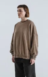 Buzo de cuello redondo color marrón claro, confeccionado en algodón premium con textura acanalada. Presenta costuras expuestas y detalles deshilachados en cuello, puños y ruedo, con un calce oversize y mangas abullonadas.
