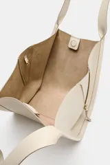 Bolso formato shopper de color beige, con detalle de pespuntes, cremalleras laterales con tiradores, doble asa y compartimento interior extraíble con cierre imantado.
