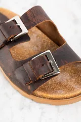 Sandalias de cuero marrón con doble tira ajustable con hebilla metálica.