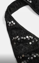 Conjunto de dos piezas negro, compuesto por un top halter con abertura frontal y detalle de hebilla dorada, y una falda larga transparente con lentejuelas plateadas dispuestas en líneas diagonales y flecos colgantes.