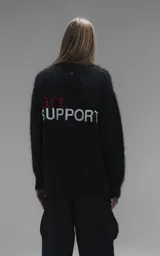 Sweater de punto negro con textura suave, cuello redondo y diseño oversize. Presenta un bordado frontal con la frase 'art SUPPORT' en letras rojas y blancas, y un pequeño detalle de tijeras bordado en la nuca.