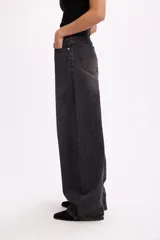 Pantalón de jean estilo baggy, de corte amplio y tiro medio, confeccionado en denim negro con textura de pana fina. Presenta diseño de cinco bolsillos, cierre frontal con botón metálico y cremallera, y perneras holgadas.